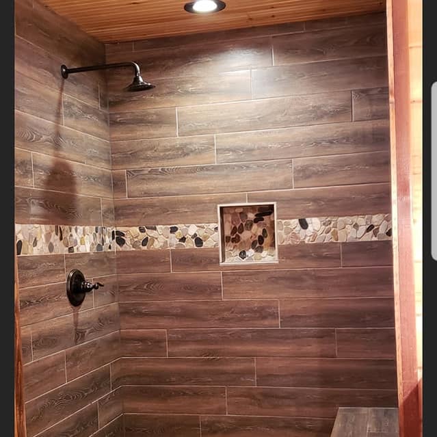 Walk-in shower finished remodel in Weatherford, TX by Prestige Plumbing & Construction featuring wood-look tile walls, decorative stone accent strip, and recessed shower niche.